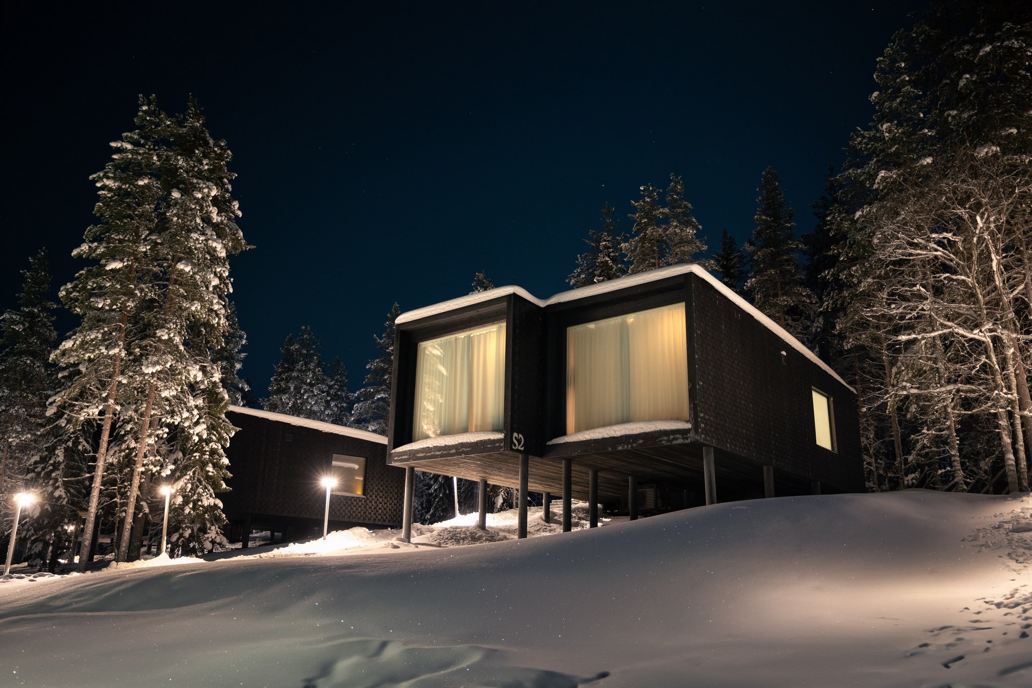 Cabin windows glowing among winter pines at Arctic TreeHouse Hotel in Rovaniemi