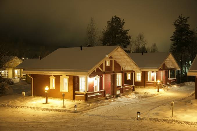Lit chalet windows on a snowy slope above Rovaniemi at Lapland Hotels Ounasvaara Chalets